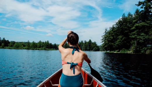 Person in swimsuit paddling in canoe on tree lined waterway.