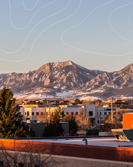 Boulder buildings in front of Rocky Mountains with topographic lines in the sky.